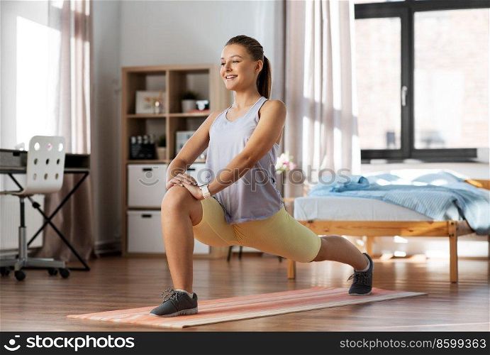 sport, fitness and healthy lifestyle concept - smiling teenage girl exercising on yoga mat and stretching leg at home. happy teenage girl exercising on yoga mat at home