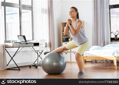 sport, fitness and healthy lifestyle concept - smiling teenage girl exercising with exercise ball at home. teenage girl training on exercise ball at home