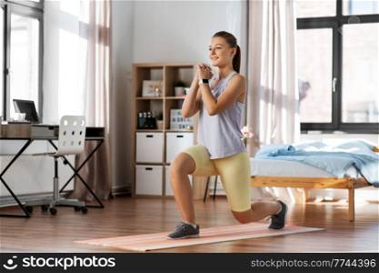 sport, fitness and healthy lifestyle concept - smiling teenage girl with smart watch exercising on yoga mat and doing low lunge at home. happy teenage girl exercising on yoga mat at home