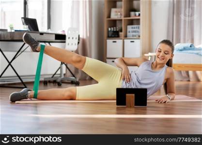 sport, fitness and healthy lifestyle concept - smiling teenage girl with tablet pc computer exercising with resistance band at home. teenage girl with tablet pc exercising at home