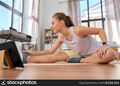 sport, fitness and healthy lifestyle concept - smiling teenage girl with tablet pc computer exercising on yoga mat at home. teenage girl with tablet pc exercising at home