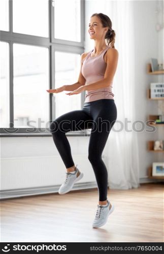 sport, fitness and healthy lifestyle concept - smiling young woman exercising and jumping at home. smiling young woman exercising at home