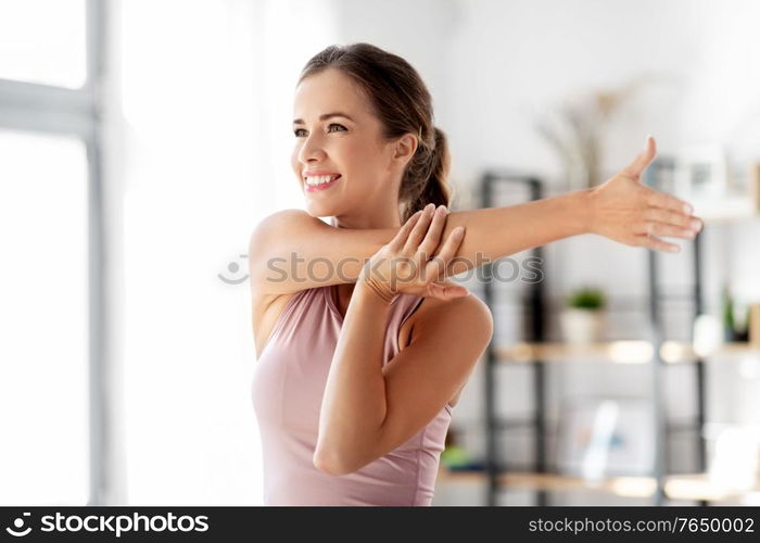 sport, fitness and healthy lifestyle concept - smiling young woman stretching arm at home. smiling young woman stretching arm at home