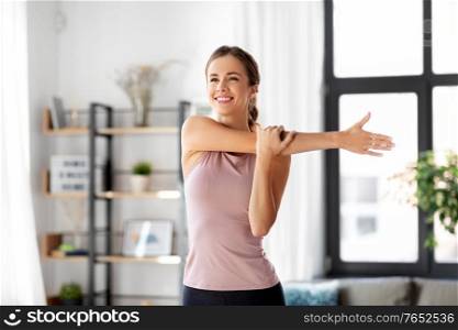 sport, fitness and healthy lifestyle concept - smiling young woman stretching arm at home. smiling young woman stretching arm at home