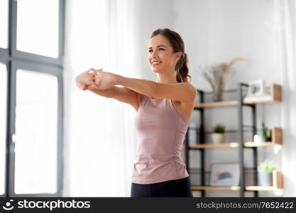 sport, fitness and healthy lifestyle concept - smiling young woman stretching arms at home. smiling young woman stretching arms at home