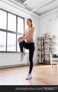 sport, fitness and healthy lifestyle concept - smiling young woman stretching leg at home. smiling young woman stretching leg at home