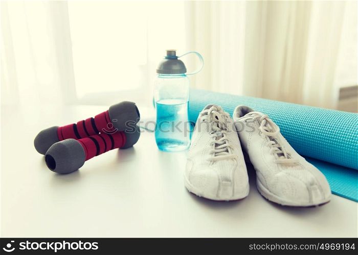 sport, fitness and objects concept - close up of bottle with water, dumbbells, sneakers and sports mat at home. close up of bottle, dumbbells, sneakers and mat
