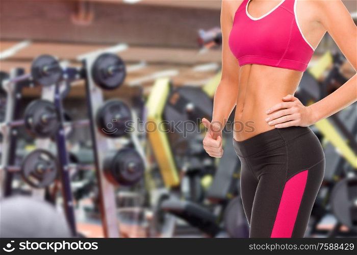 sport, fitness and people - close up of fit woman showing thumbs up over gym background. close up of fit woman showing thumbs up over gym