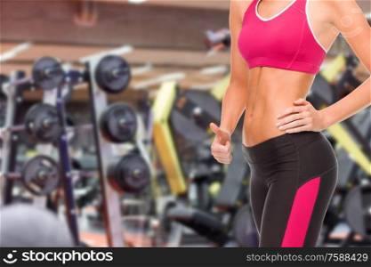 sport, fitness and people - close up of fit woman showing thumbs up over gym background. close up of fit woman showing thumbs up over gym