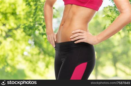 sport, fitness and people - close up of slim fit woman&rsquo;s body with trained abs over green natural background. close up of slim fit woman&rsquo;s body with trained abs