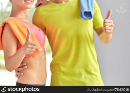 sport, fitness and people concept - close up of happy couple with towels showing thumbs up in gym. close up of happy couple showing thumbs up in gym