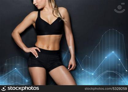 sport, fitness and people concept - close up of young woman in sportswear posing over black background with diagram chart hologram. close up of woman in black sportswear posing