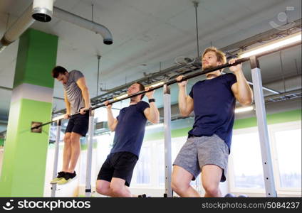 sport, fitness and people concept - group of young men exercising and doing pull-ups on horizontal bar in gym. group of young men doing pull-ups in gym. group of young men doing pull-ups in gym