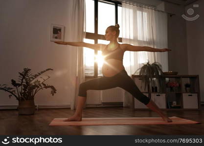 sport, fitness and people concept - happy pregnant woman doing yoga warrior pose at home over sunshine. pregnant woman doing yoga at home over sunshine