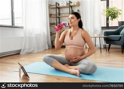 sport, fitness and people concept - happy pregnant woman drinking water after yoga at home. pregnant woman drinking water after yoga at home