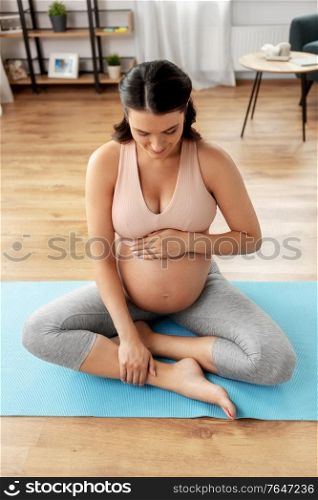 sport, fitness and people concept - happy pregnant woman sitting on yoga mat at home. happy pregnant woman sitting on yoga mat at home