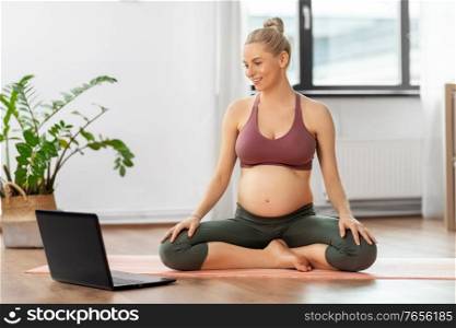 sport, fitness and people concept - happy pregnant woman with laptop computer doing yoga at home. pregnant woman with laptop doing yoga at home