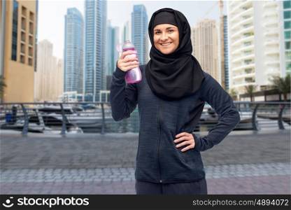 sport, fitness and people concept - happy smiling muslim woman in hijab with water bottle over dubai city street background