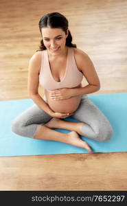 sport, fitness and people concept - happy smiling pregnant woman sitting on yoga mat at home. happy pregnant woman sitting on yoga mat at home