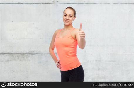 sport, fitness and people concept - happy smiling sportive young woman showing thumbs up over concrete wall background. happy sportive young woman showing thumbs up