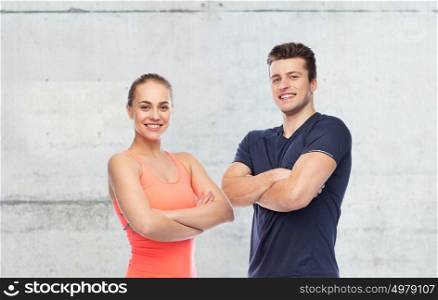 sport, fitness and people concept - happy sportive man and woman over concrete wall background. happy sportive man and woman