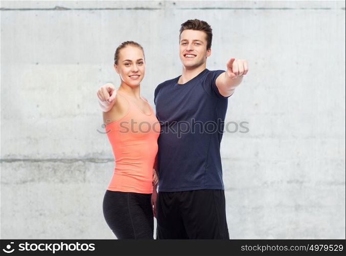 sport, fitness and people concept - happy sportive man and woman pointing finger on you over concrete wall background. happy sportive man and woman pointing finger