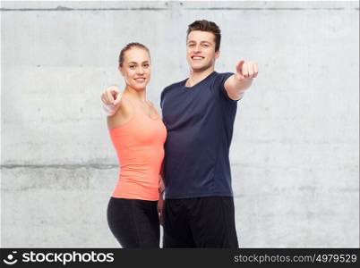 sport, fitness and people concept - happy sportive man and woman pointing finger on you over concrete wall background. happy sportive man and woman pointing finger