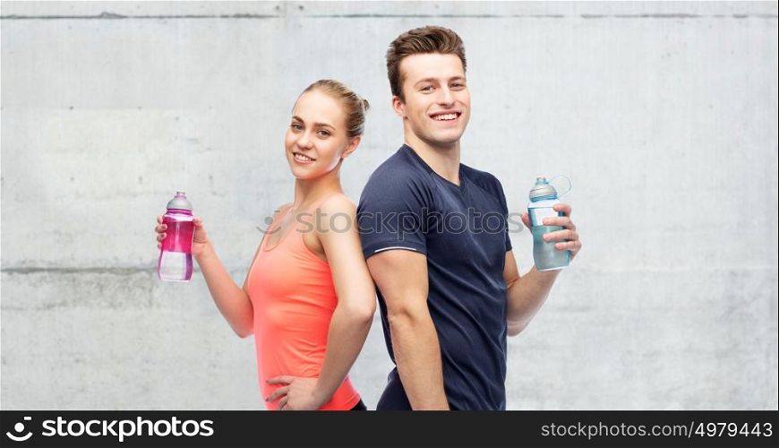 sport, fitness and people concept - happy sportive man and woman with water bottles over concrete wall background. sportive man and woman with water bottles