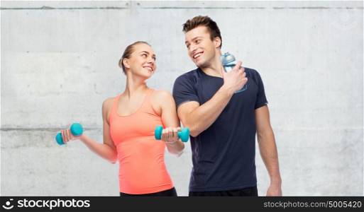 sport, fitness and people concept - happy sportive man and woman with dumbbell and water bottle over concrete wall background. sportive man and woman with dumbbell and water
