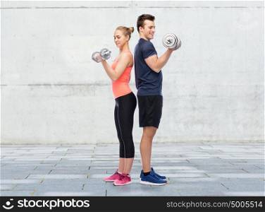 sport, fitness and people concept - happy sportive man and woman with dumbbells flexing muscles over concrete wall background. sportive man and woman with dumbbells