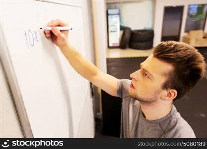 sport, fitness and people concept - man writing numbers to whiteboard in gym. man writing numbers to whiteboard in gym