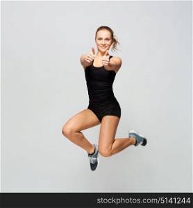 sport, fitness and people concept - young woman in black sportswear jumping and showing thumbs up. woman in sportswear jumping and showing thumbs up