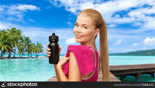 sport, fitness and people - happy smiling woman with bottle and towel over tropical beach background in french polynesia. happy smiling woman with sports bottle and towel
