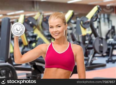 sport, fitness and people - happy smiling young sporty woman with heavy dumbbell exercising over gym on background. happy young woman with dumbbell exercising in gym
