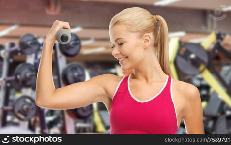 sport, fitness and people - happy smiling young sporty woman with light dumbbells exercising over gym on background. happy young woman with dumbbells exercising in gym