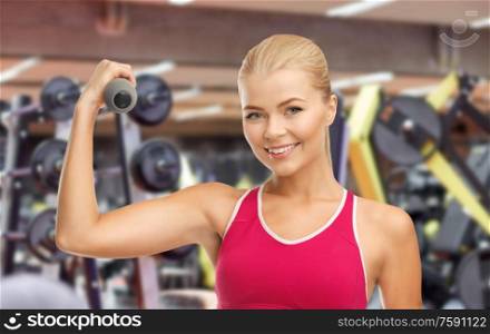 sport, fitness and people - happy smiling young sporty woman with light dumbbells exercising over gym on background. happy young woman with dumbbells exercising in gym