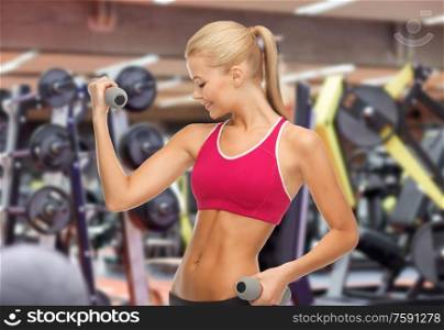 sport, fitness and people - happy smiling young sporty woman with light dumbbells exercising over gym on background. happy young woman with dumbbells exercising in gym