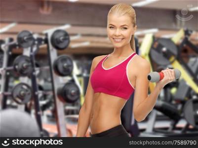 sport, fitness and people - happy smiling young sporty woman with light dumbbells over gym background. happy woman training with light dumbbells in gym