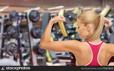 sport, fitness and people - young sporty woman showing her biceps over gym on background. young sporty woman showing her biceps in gym