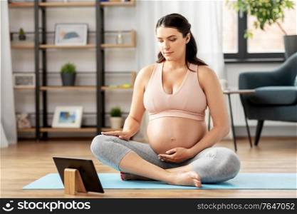 sport, fitness and technology concept - happy pregnant woman with tablet pc computer doing yoga at home. pregnant woman with tablet pc doing sports at home
