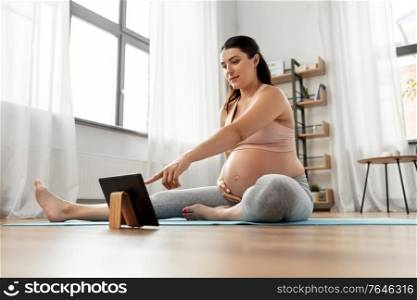 sport, fitness and technology concept - happy pregnant woman with tablet pc computer exercising at home. pregnant woman with tablet pc doing sports at home