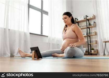 sport, fitness and technology concept - happy pregnant woman with tablet pc computer exercising at home. pregnant woman with tablet pc doing sports at home