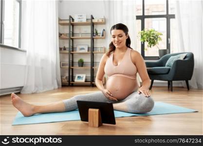 sport, fitness and technology concept - happy smiling pregnant woman with tablet pc computer exercising at home. pregnant woman with tablet pc doing sports at home