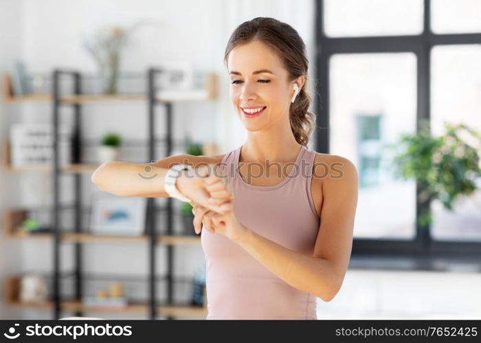 sport, fitness and technology concept - happy smiling young woman with smart watch and earphones exercising at home. woman with smart watch and earphones doing sports