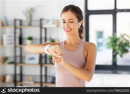sport, fitness and technology concept - happy smiling young woman with smart watch and earphones exercising at home. woman with smart watch and earphones doing sports