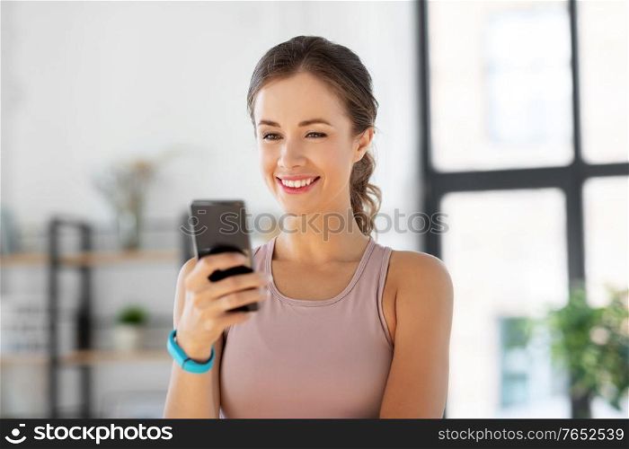 sport, fitness and technology concept - happy smiling young woman with smatphone exercising at home. young woman with smatphone exercising at home