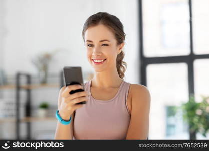 sport, fitness and technology concept - happy smiling young woman with smatphone exercising at home. young woman with smatphone exercising at home