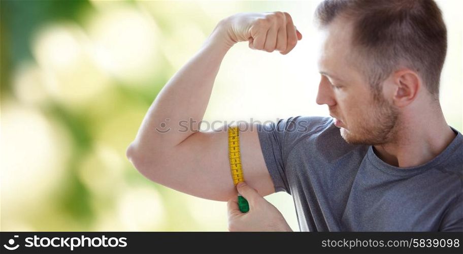 sport, fitness, bodybuilding and people concept - close up of male hands with tape measuring bicep over green natural background