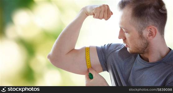 sport, fitness, bodybuilding and people concept - close up of male hands with tape measuring bicep over green natural background