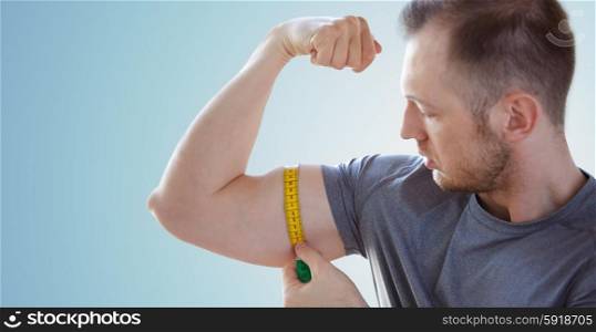 sport, fitness, bodybuilding and people concept - close up of male hands with tape measuring bicep over blue background